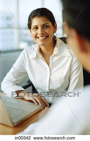 Stock Image - Female executive smiling at man facing her, over the shoulder view. Fotosearch