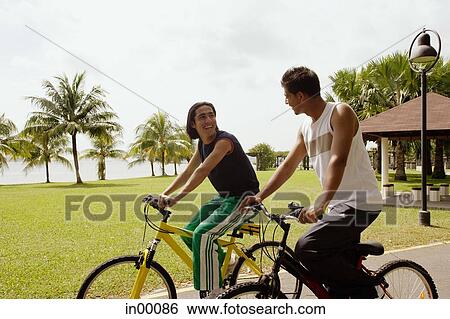 Friends cycling side by side in park View Large Photo Image Stock Photograph - Friends cycling side by side in park. Fotosearch