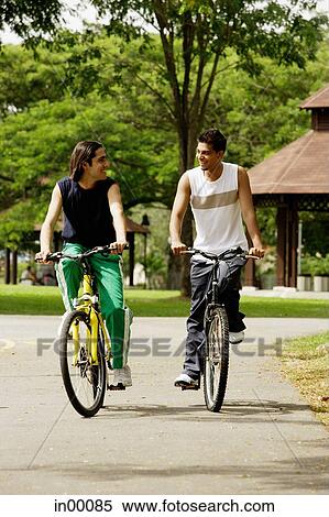 Friends cycling side by side in park View Large Photo Image Stock Photography - Friends cycling side by side in park. Fotosearch