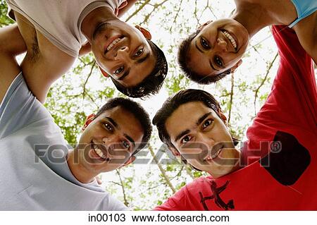Stock Image - Group of friends, arms around each other, looking down at camera. Fotosearch