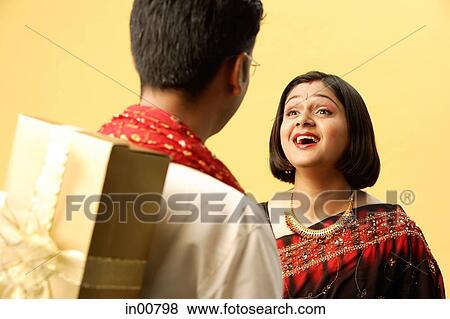Indian couple in traditional clothing, standing face to face, man hiding gift behind back View Large Photo Image Stock Photo - Indian couple in traditional clothing, standing face to face, man hiding gift behind back. Fotosearch