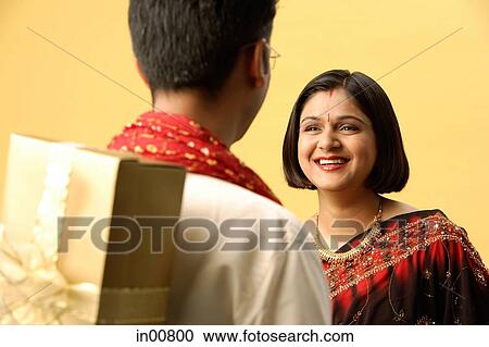 Indian couple standing face to face, man hiding gift behind back, woman smiling View Large Photo Image Stock Image - Indian couple standing face to face, man hiding gift behind back, woman smiling. Fotosearch