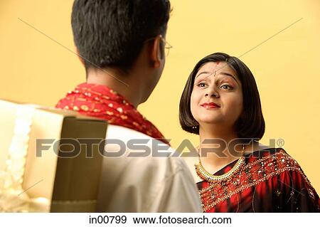 Indian couple standing face to face, man hiding gift behind back View Large Photo Image Stock Photo - Indian couple standing face to face, man hiding gift behind back. Fotosearch