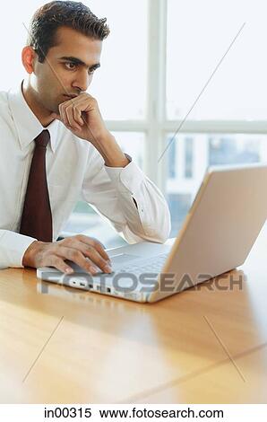 Stock Photography - Male executive looking at laptop, hand on chin, portrait. Fotosearch