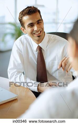 Stock Photograph - Male executive sitting across from another person, smiling, over the shoulder view. Fotosearch