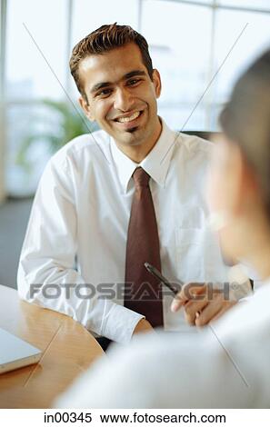 Stock Photography - Male executive smiling at person in front of him, over the shoulder view. Fotosearch