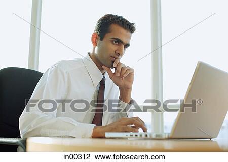 Male executive using laptop, hand on chin View Large Photo Image Stock Image - Male executive using laptop, hand on chin. Fotosearch