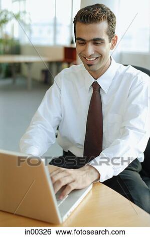 Stock Photograph - Male executive using laptop, smiling. Fotosearch