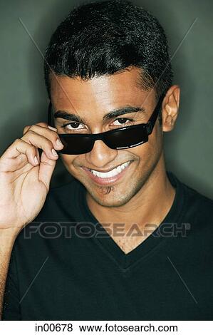 Stock Photo - Man adjusting sunglasses, looking at camera. Fotosearch