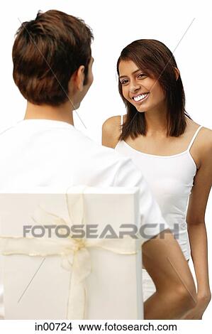 Picture - Man holding present behind his back, woman smiling in front of him. Fotosearch