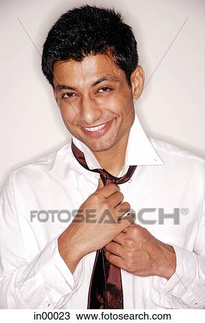 Stock Image - Man looking at camera, fixing tie. Fotosearch