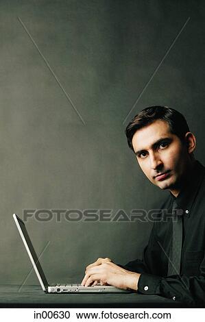 Stock Image - Man looking at camera, laptop open in front of him. Fotosearch