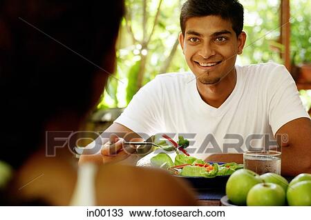 Stock Image - Man looking at person opposite him, salad in front of him. Fotosearch