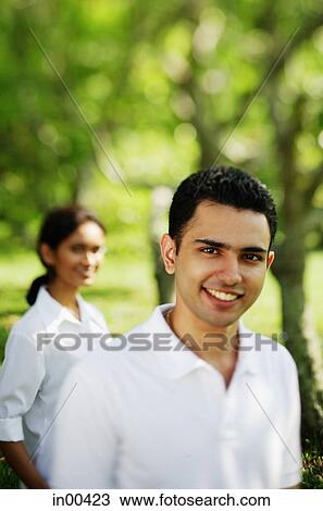 Stock Image - Man smiling at camera, woman in the background. Fotosearch