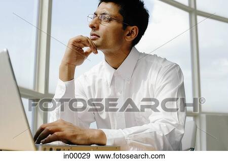 Stock Photo - Man using laptop, hand on chin, looking away. Fotosearch