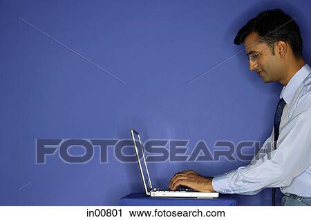 Stock Image - Man using laptop, side view. Fotosearch