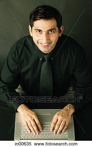 Man using laptop, smiling up at camera View Large Photo Image Stock Photography - Man using laptop, smiling up at camera. Fotosearch