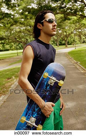 Man wearing sunglasses, holding skateboard View Large Photo Image Stock Photo - Man wearing sunglasses, holding skateboard. Fotosearch