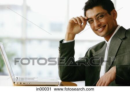 Man with hand on head, looking at camera, laptop on table View Large Photo Image Stock Image - Man with hand on head, looking at camera, laptop on table. Fotosearch