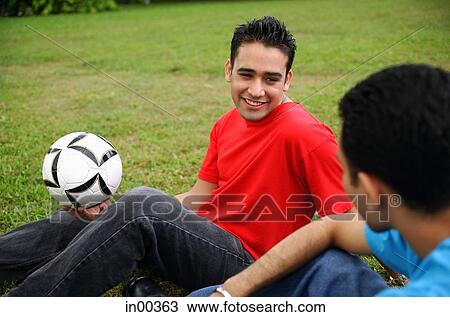 Two men sitting on grass, one holding soccer ball View Large Photo Image Stock Image - Two men sitting on grass, one holding soccer ball. Fotosearch