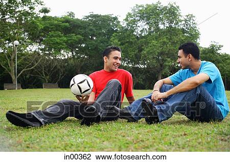 Two men sitting on grass, talking, one holding soccer ball View Large Photo Image Stock Image - Two men sitting on grass, talking, one holding soccer ball. Fotosearch