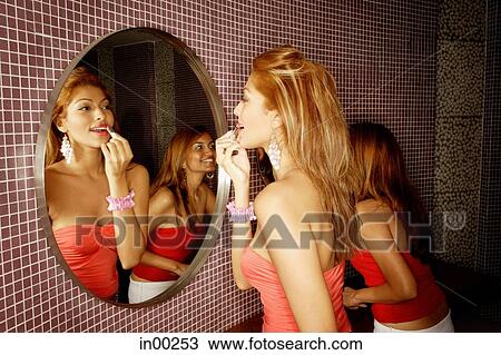 Stock Image - Two women looking at mirror, applying make-up. Fotosearch
