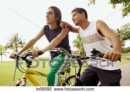 Two young men on bicycles, one leaning on the other, pointing View Large Photo Image Stock Image - Two young men on bicycles, one leaning on the other, pointing. Fotosearch