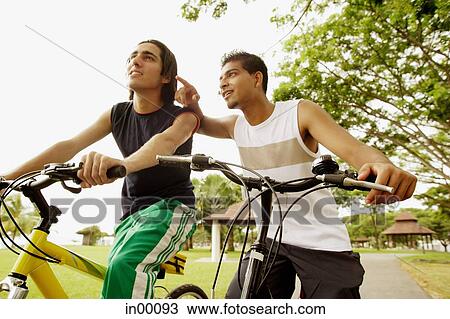 Two young men on bicycles, one pointing View Large Photo Image Stock Image - Two young men on bicycles, one pointing. Fotosearch