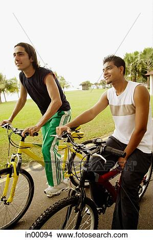 Picture - Two young men sitting on bicycles, looking away. Fotosearch