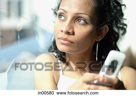 Woman holding mobile phone, looking out the window View Large Photo Image Stock Image - Woman holding mobile phone, looking out the window. Fotosearch