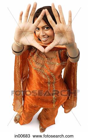 Stock Image - Woman in Indian clothing, holding hands up and looking at camera through them. Fotosearch