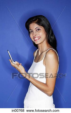 Woman looking at camera, holding mobile phone View Large Photo Image Stock Photo - Woman looking at camera, holding mobile phone. Fotosearch
