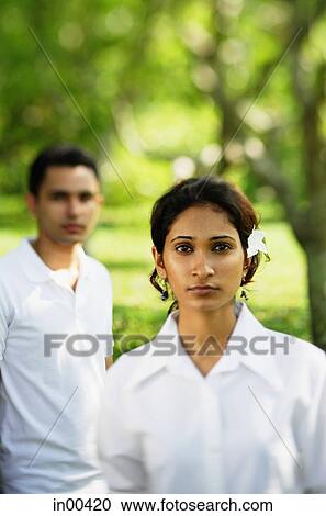 Stock Image - Woman looking at camera, man in the background. Fotosearch