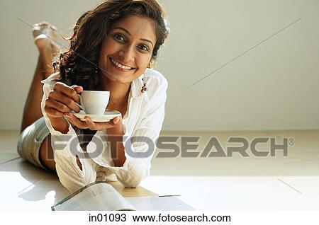 Woman lying on front, holding cup and saucer, smiling View Large Photo Image Stock Image - Woman lying on front, holding cup and saucer, smiling. Fotosearch