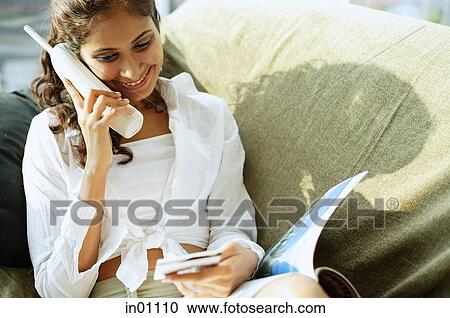 Stock Image - Woman sitting, using cordless phone. Fotosearch