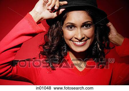 Stock Photo - Woman smiling at camera, adjusting hat on head. Fotosearch
