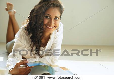 Stock Image - Woman smiling at camera, flipping through magazine. Fotosearch
