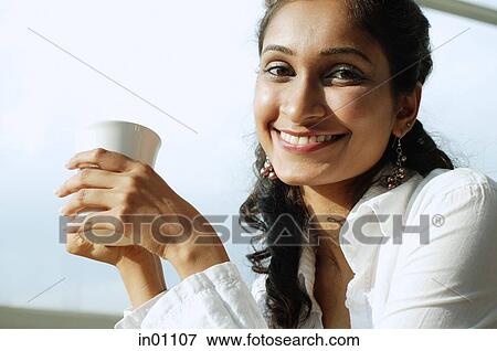 Stock Photo - Woman smiling at camera, mug in hand. Fotosearch