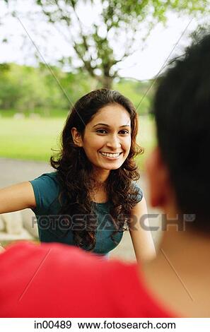 Stock Photo - Woman smiling, facing another person, over the shoulder view. Fotosearch