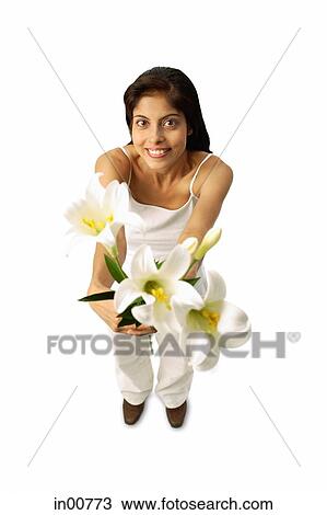 Stock Image - Woman standing, holding flowers, looking at camera. Fotosearch