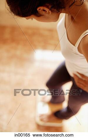 Stock Photography - Woman standing on weight scale, looking down. Fotosearch