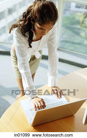 Woman standing over desk, using laptop View Large Photo Image Stock Photo - Woman standing over desk, using laptop. Fotosearch