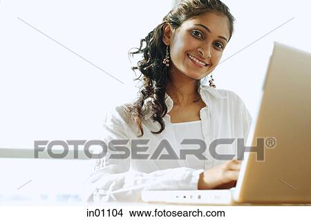 Picture - Woman using laptop, smiling at camera. Fotosearch