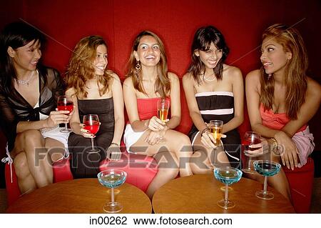 Stock Image - Women sitting side by side, holding drinks. Fotosearch