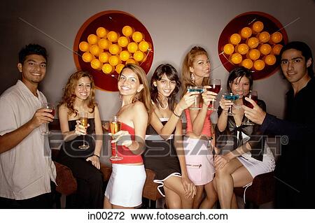 Stock Image - Young adults in night club, holding drinks out towards camera. Fotosearch