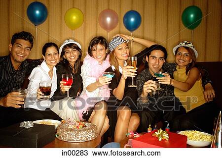 Stock Image - Young adults sitting side by side, celebrating, holding drinks. Fotosearch