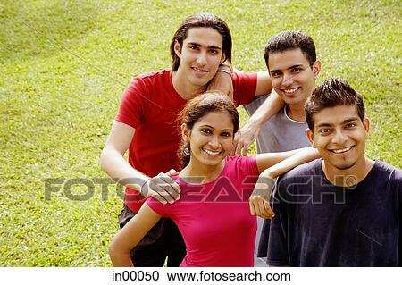 Stock Image - Young adults standing together, looking at camera, smiling. Fotosearch
