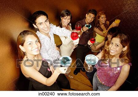 Stock Image - Young adults toasting with drinks, looking at camera. Fotosearch