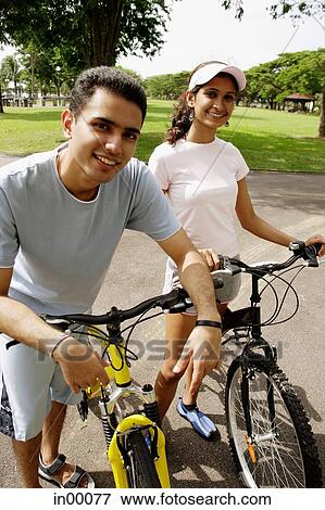 Stock Photo - Young man and woman, on bicycles, looking at camera. Fotosearch