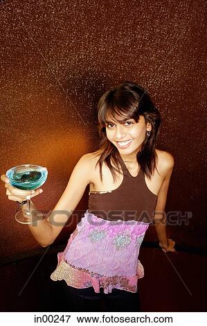 Stock Photo - Young woman holding drink, smiling at camera. Fotosearch